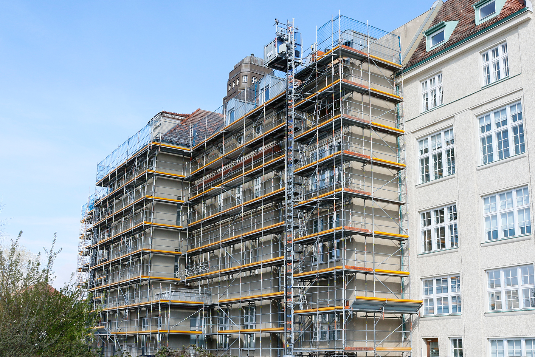 Seitenansicht des eingerüsteten Baudenkmals mit Bauaufzug und Schutznetzen – Gerüstbau Berlin Lichtenberg von Ro²